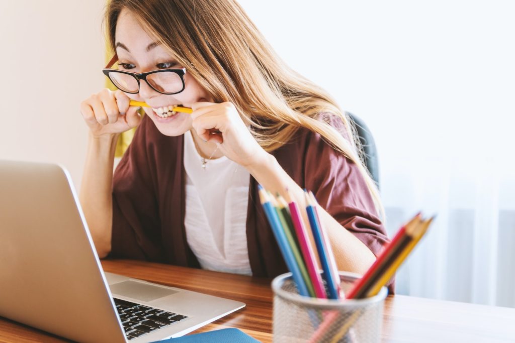 A professional woman biting pencil feeling stuck and demotivated in her Agile role while sitting on chair in front of computer during daytime